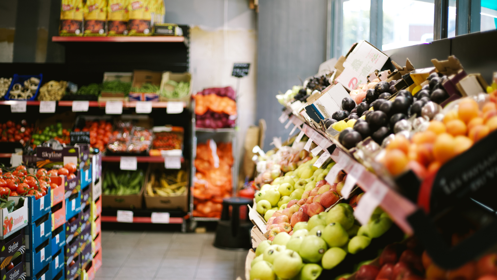 Grocery store produce section featuring stacks of fresh items like tomatoes, apples